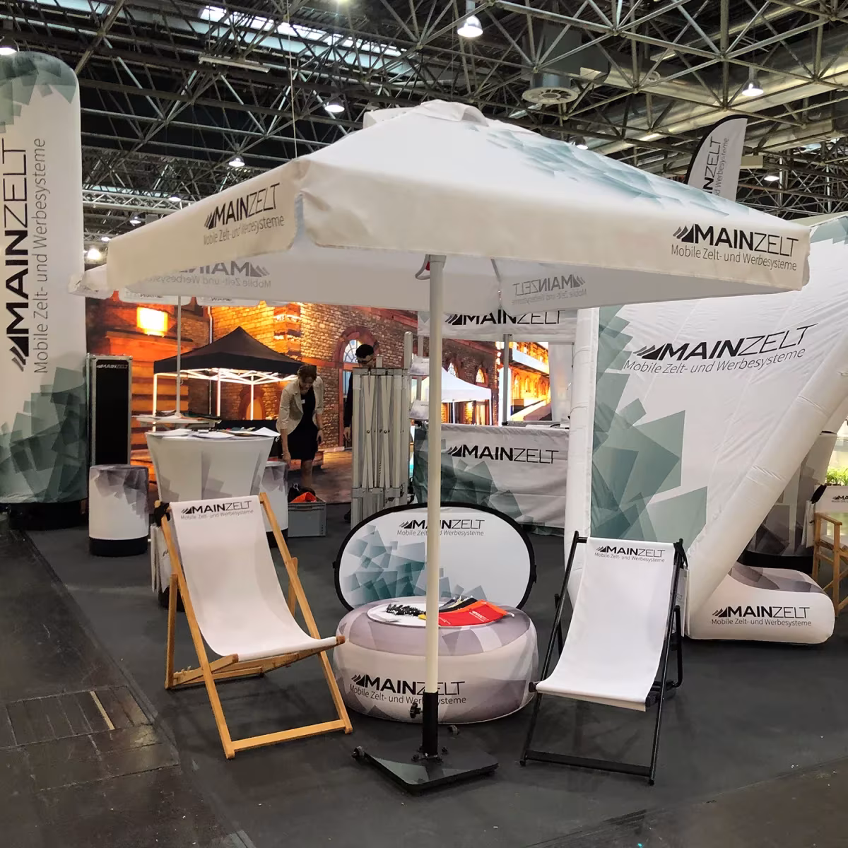 Liegestühle aus Holz und Aluminium unter einem Sonnenschirm am Messestand