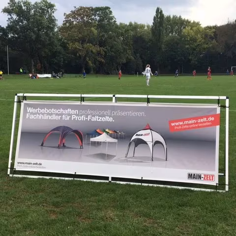 Werbebande am Rand eines Fußballplatzes mit Faltzelt-Motiv