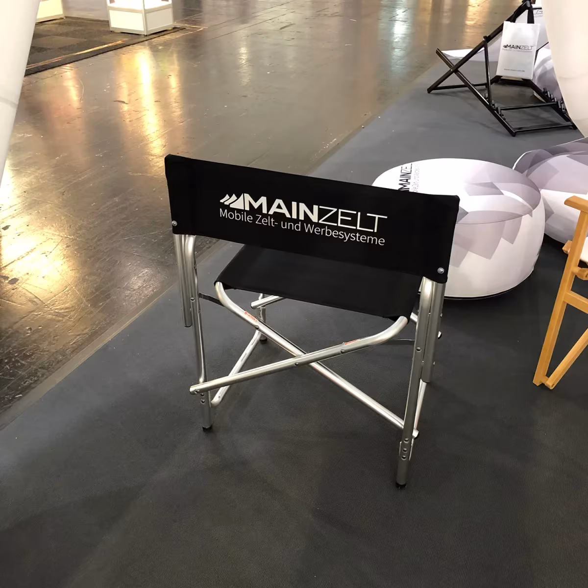 Regiestuhl mit Logo auf der Rückenlehne in einer Messehalle