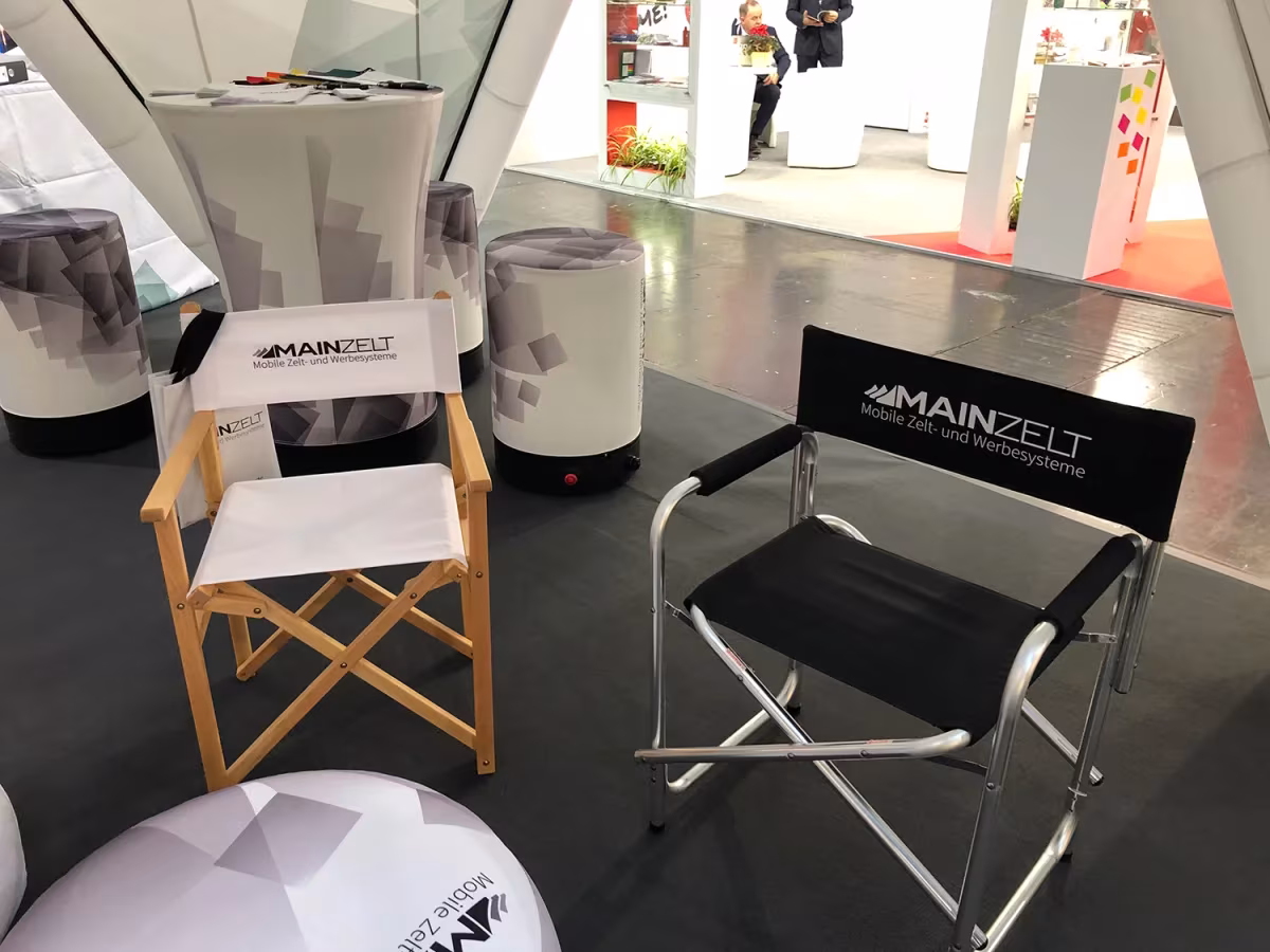 Regiestuhl aus Holz neben einem Regiestuhl aus Aluminium am Messestand